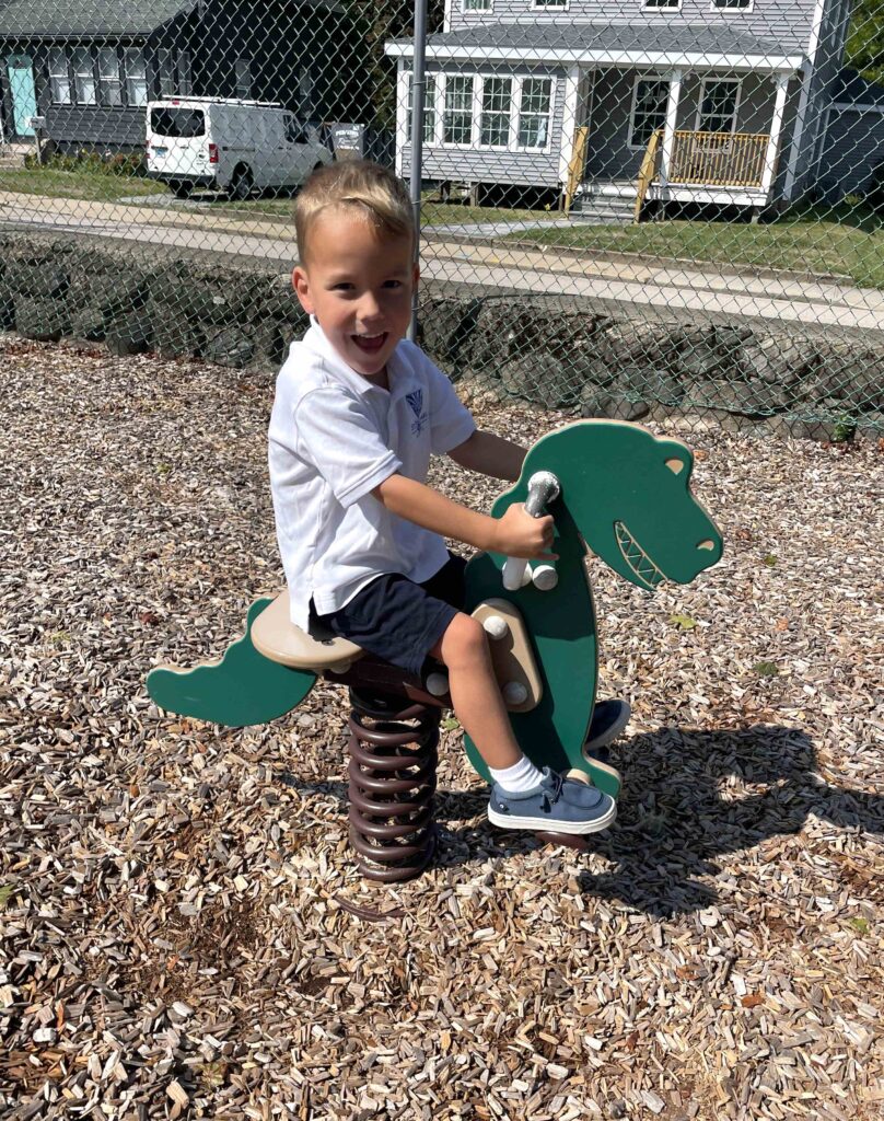 Smiling boy in school uniform playing on green playground horse