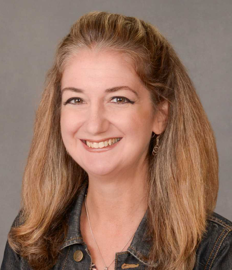 Smiling woman with long light brown hair wearing a dark denim jacket