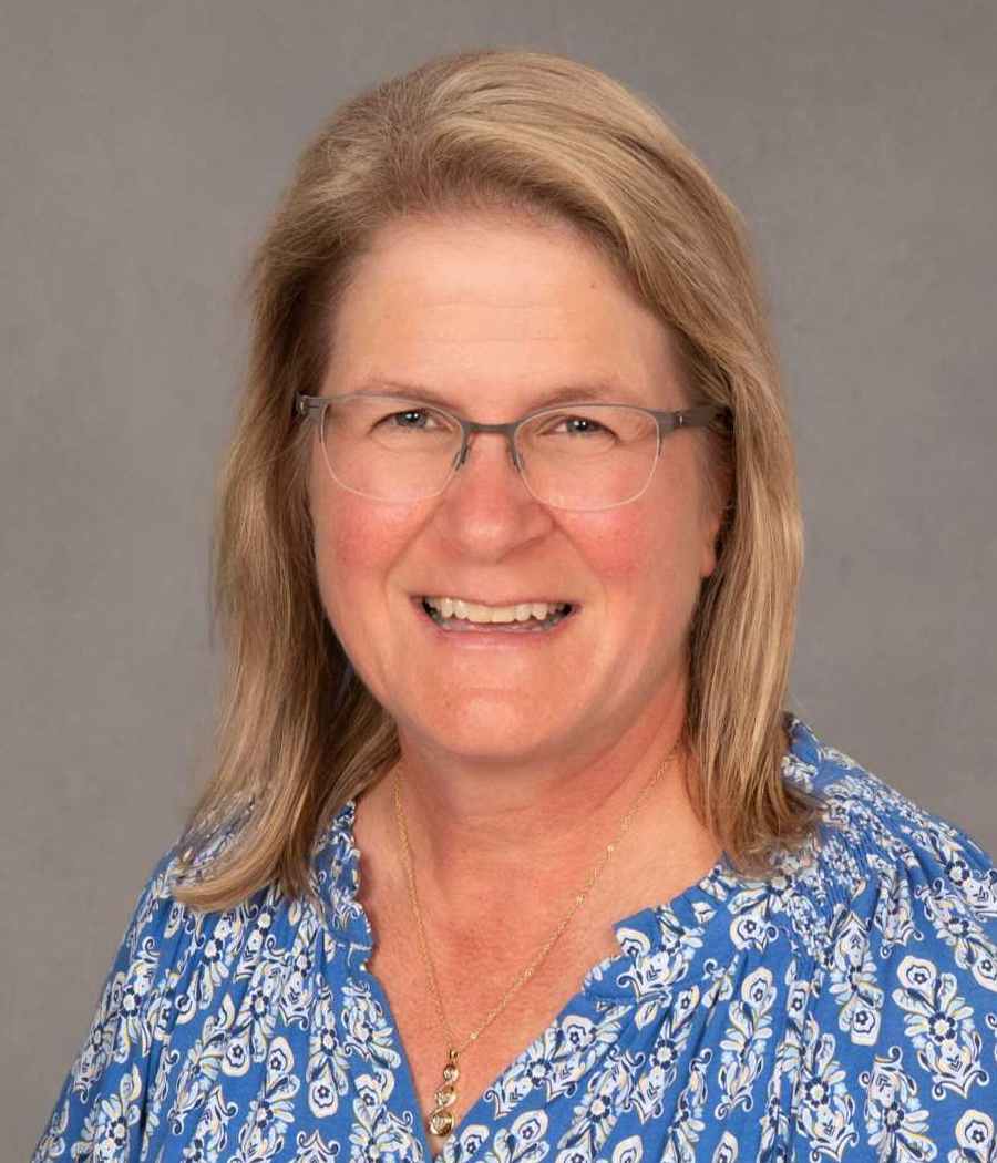 Smiling woman with blonde hair wearing light colored glasses and a blue and white patterned shirt