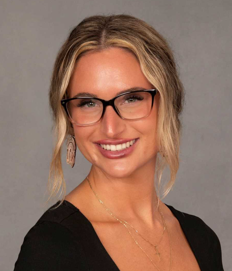 Smiling woman with blonde pony tail with dark glasses wearing a black sweater