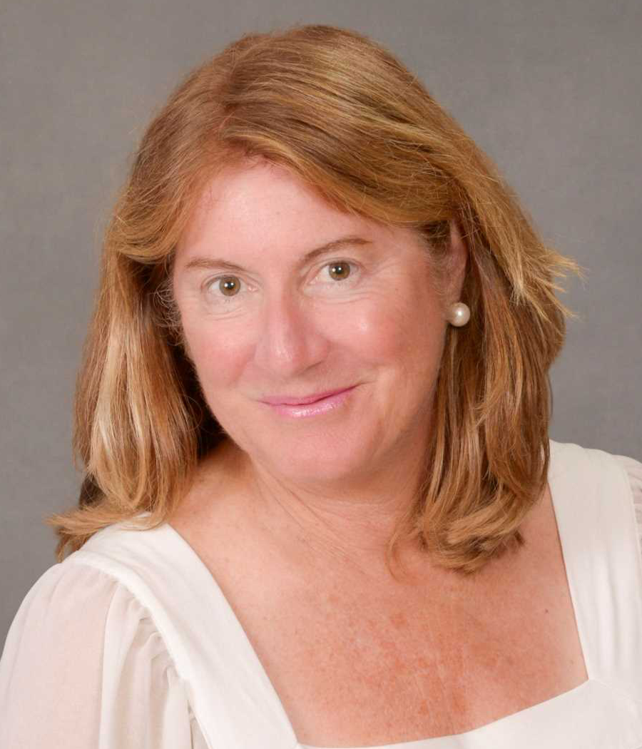 Smiling woman with light brown hair wearing a white shirt and pearl earrings