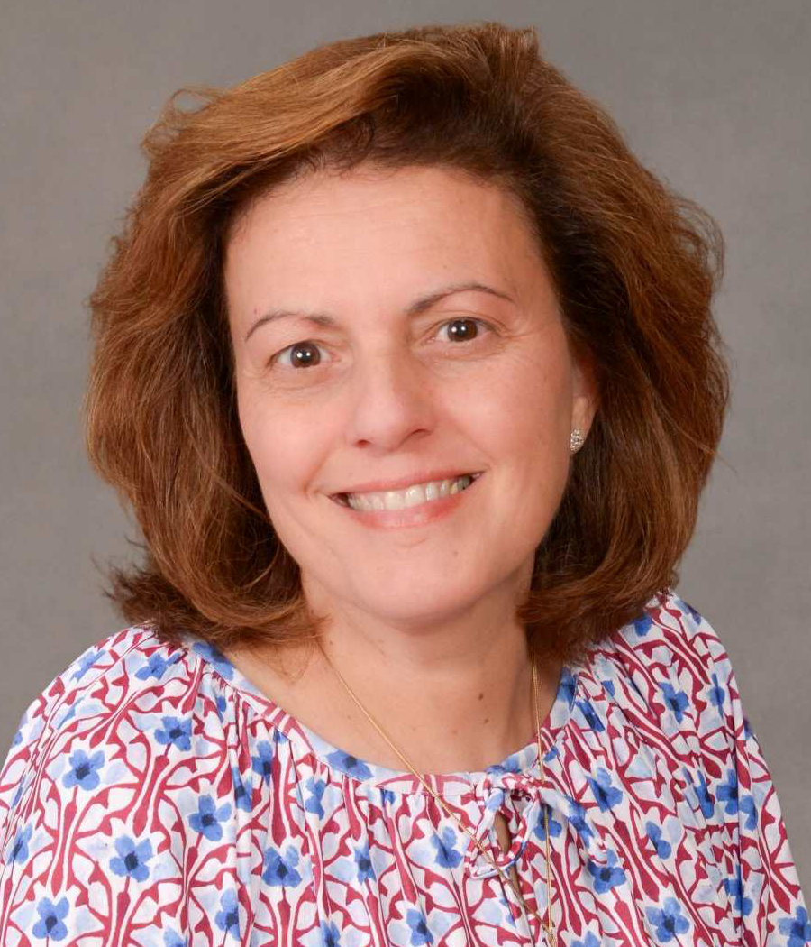 Smiling woman with short brown hair wearing a white shirt with red pattern and blue flowers