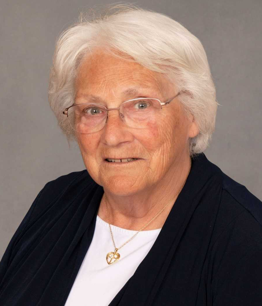 Smiling woman with short white hair wearing light glasses, white shirt and black jacket