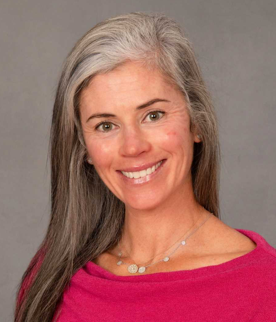 Smiling woman with long gray and light brown hair wearing a bright pink sweater
