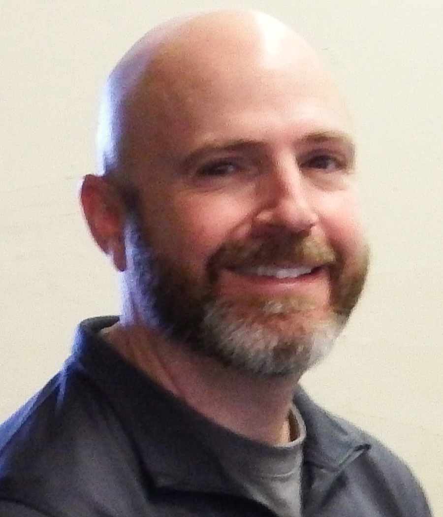 smiling man with shaved head and beard with dark blue shirt