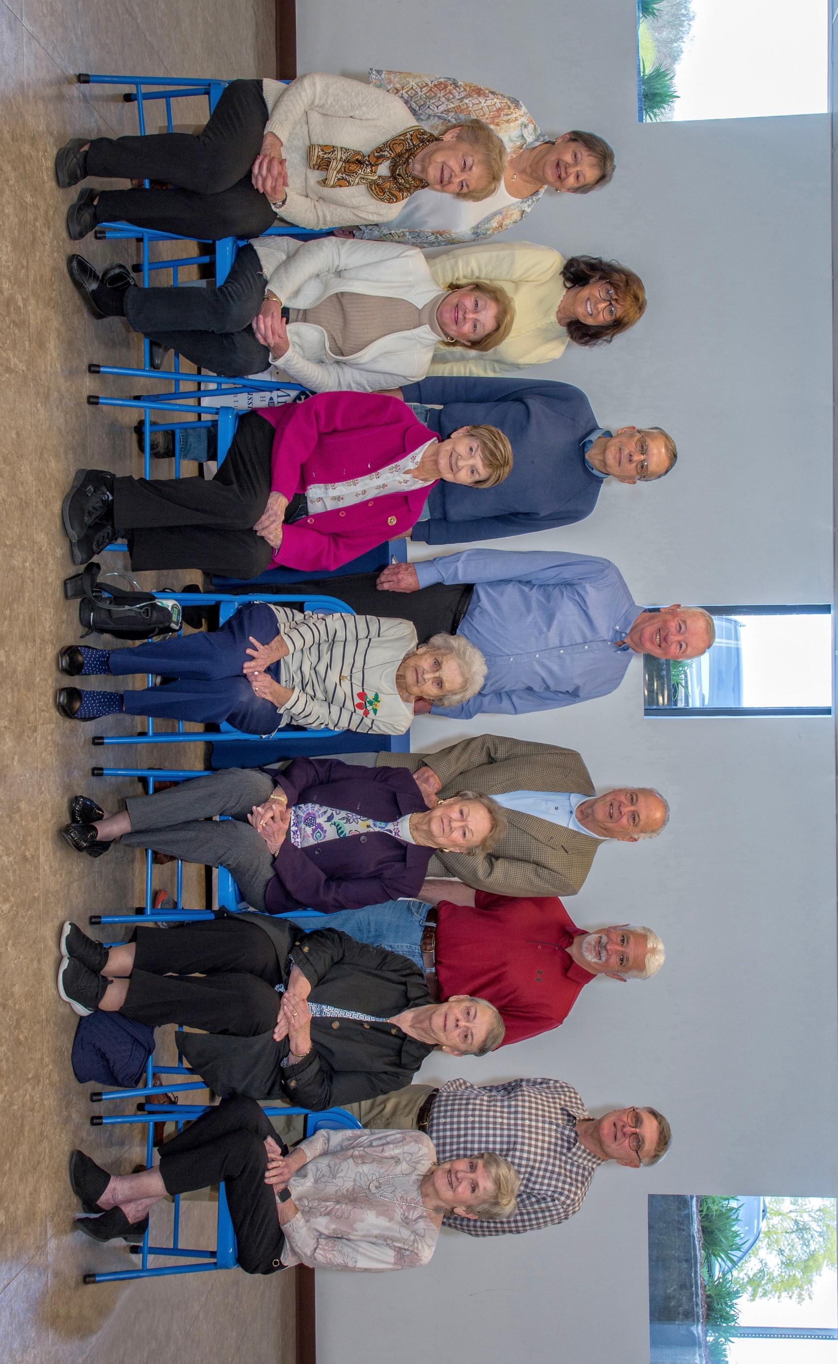 Small group of men and women formally standing and sitting and smiling at camera with light gray background and tan tile floors