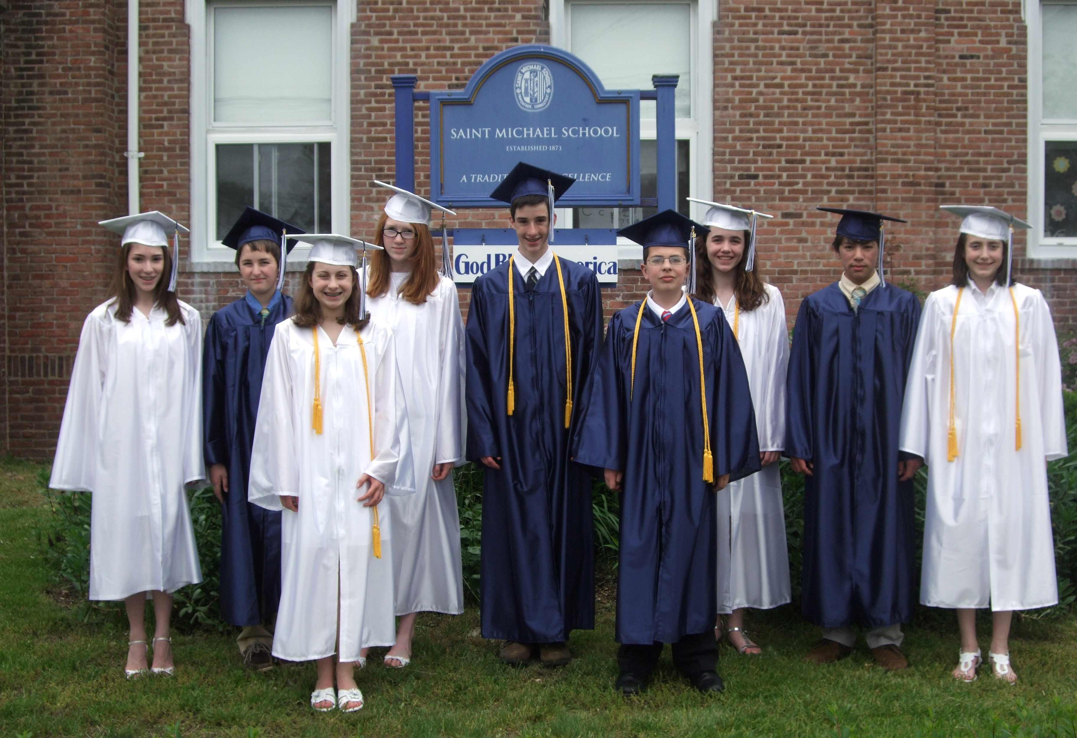 Photo from 2011 in front a brick building with a blue sign of a group young men in blue graduation caps and gowns and young women in white graduation caps and gowns