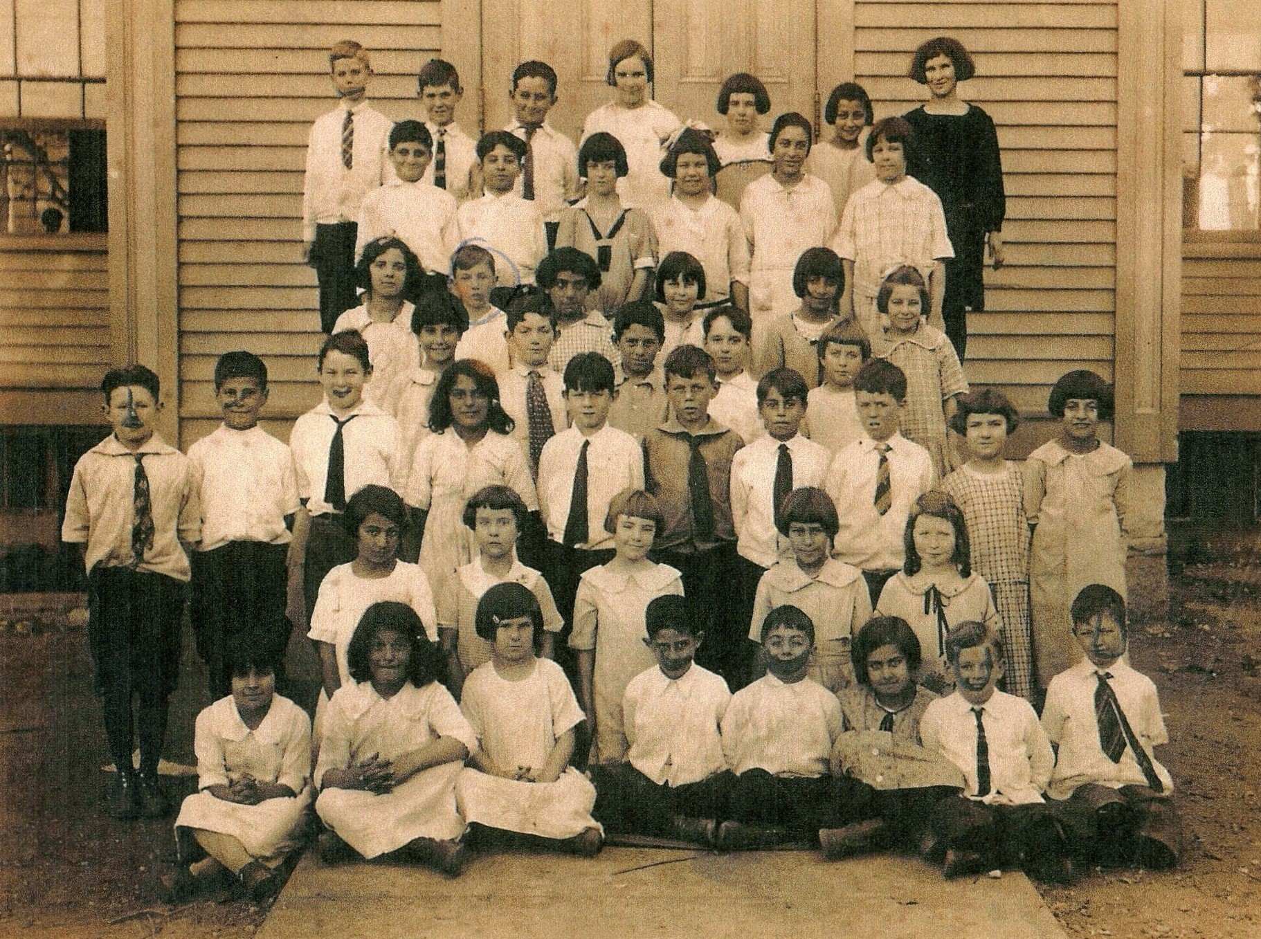 Black and white photo in front of building from 1925 of children in dress clothes with a woman in a dark dress