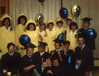 Photo from 1987 of a group young men in blue graduation caps and gowns and young women in yellow graduation caps and gowns with blue and yellow balloons